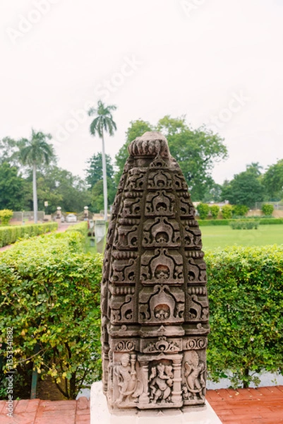 Fototapeta Ancient stone sculpture in Sarnath, Varanasi, with detailed carvings of deities and motifs, set in a lush garden landscape.