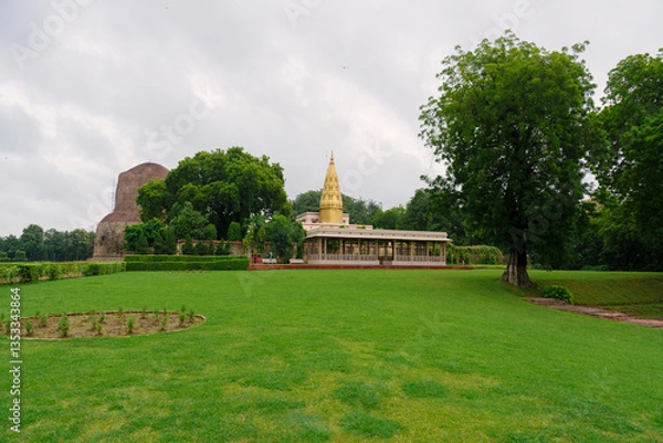 Fototapeta Dhamek Stupa and nearby golden spire temple in Sarnath, Varanasi, surrounded by lush green lawns and peaceful trees.