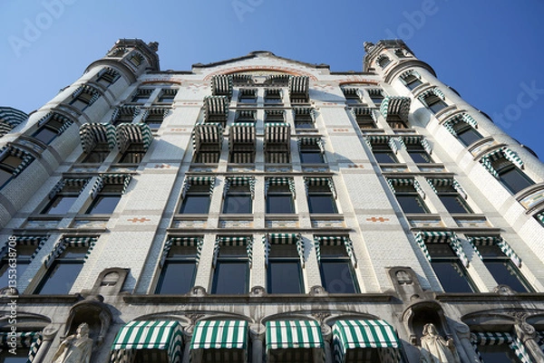 Fototapeta The facade of a historic building in Rotterdam with intricate architectural details, view from a low angle against a clear blue sky.