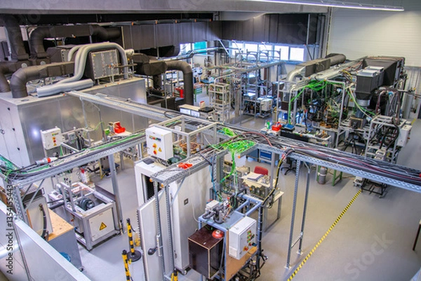 Fototapeta Wide view of advanced industrial automation laboratory with control panels, machinery, cable trays, and testing stations used for engineering research and factory system development.