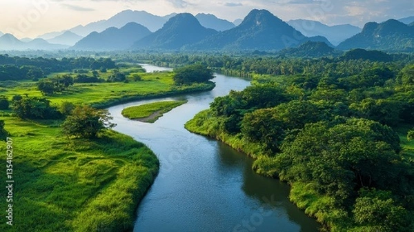Fototapeta Serene River Flowing Through Lush Green Landscape Surrounded by Majestic Mountains Under a Blue Sky at Sunset