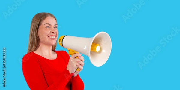 Fototapeta Young woman enthusiastically holding a megaphone against bright blue background, ready to make  statement during  vibrant gathering or event