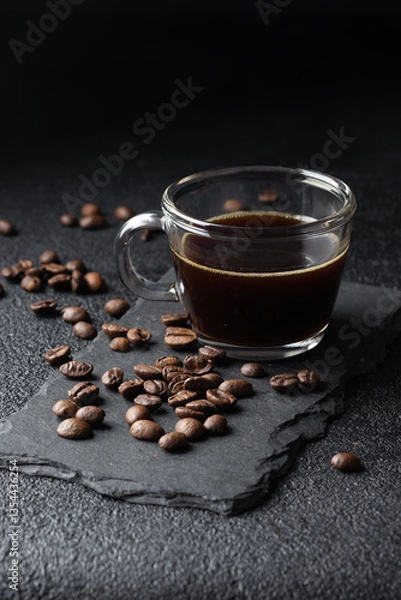 Fototapeta Dark coffee in a glass coffee cup, black espresso and roasted coffee beans pilled on black table, close up. Vertical banner with copy space