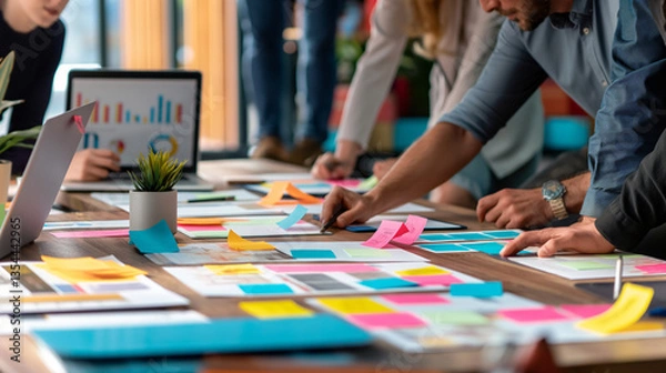 Fototapeta Collaboration in the office with colleagues brainstorming ideas, reviewing colorful sticky notes and documents on a table,