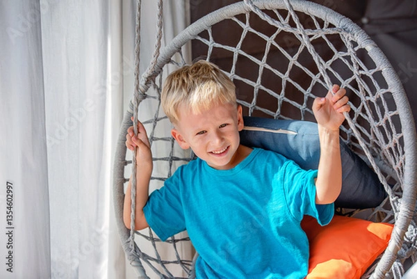 Fototapeta A portrait of a five-year-old blond-haired boy on a wicker swing.