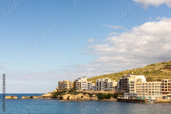 Obraz Coastal buildings in Xlendi Bay, Gozo, Malta. A scenic view of modern seaside buildings along the rocky coastline of Xlendi Bay, Gozo, Malta, with a clear blue sky and Mediterranean waters