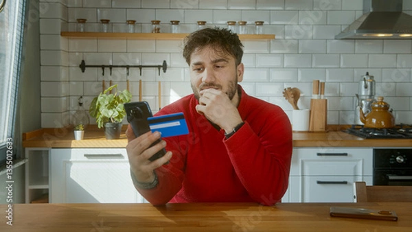 Obraz Man Making an Online Payment with a Credit Card and Smartphone in a Modern Kitchen