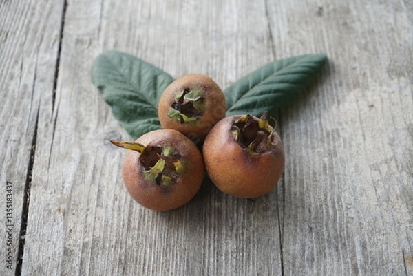 Fototapeta Three Ripe Medlar Fruits Placed on a Wooden Table in Natural Light