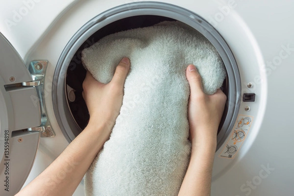Fototapeta hand and puts the laundry into the washing machine