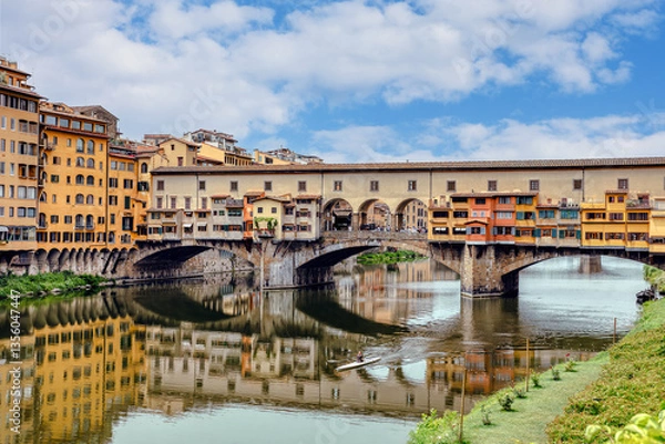 Fototapeta The Ponte Vecchio bridge in Florence showcases its colorful buildings and shops reflecting in the tranquil waters Arno river.