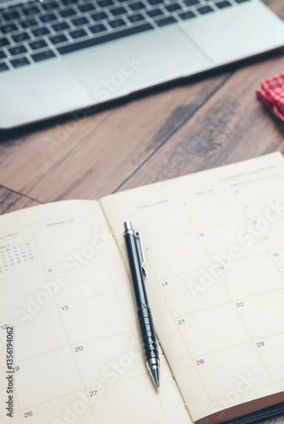 Fototapeta Calendar Planner book to plan reminder for daily appointment timetable, appointment, organization, and meeting agenda for job on wooden desk and working from home-vertical image.