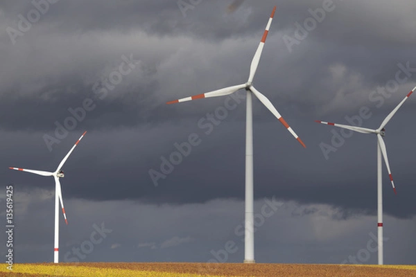 Fototapeta Three wind turbines in the field on dark gloomy day