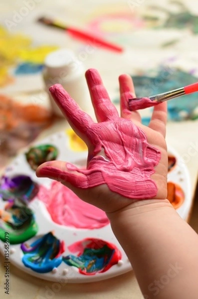 Obraz Child painting her hand with pink paint and background with palette of colorful paint