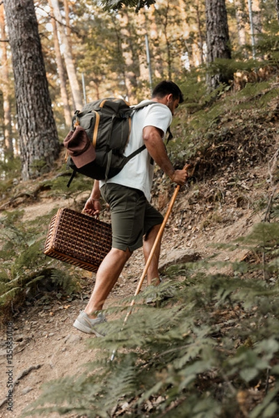 Obraz Adult man climbing a forest trail with a backpack and walking stick