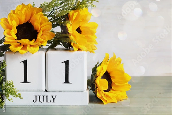 Fototapeta World Population Day.  White wood calendar blocks with the date July 11th and beautiful sunflower bouquet with bokeh. Selective focus with blurred background. 