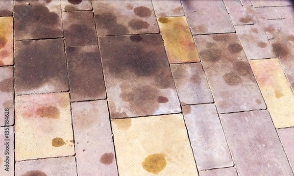 Fototapeta Stained paving tiles with dark and rusty spots, possibly caused by oil, rust, or water damage. Ideal for illustrating surface contamination or cleaning challenges. High quality photo