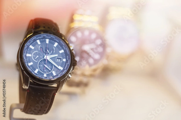 Fototapeta Beautiful black leather watch in front of other watches. Lens flare in background.