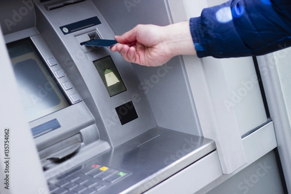 Fototapeta Hand of a man with a credit card, using an ATM. Man using an atm machine with his credit card.