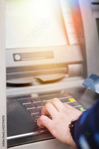 Fototapeta Hand of a man with a credit card, using an ATM. Man using an atm machine with his credit card.