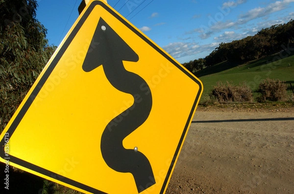 Obraz A windy road is warned by a big yellow sign