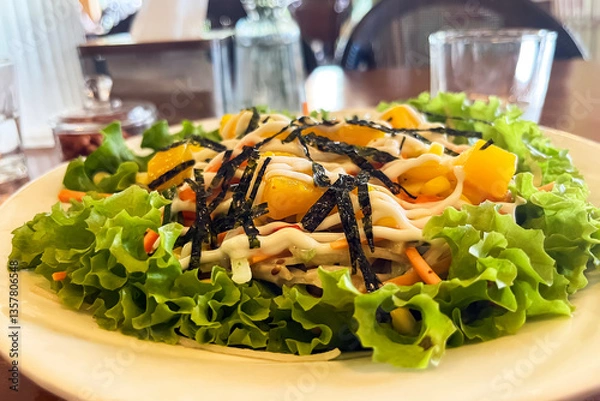 Fototapeta Kani salad with crab, fresh lettuce and mango with vegetables on a plate in a cafe