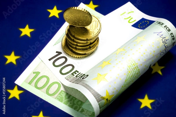 Fototapeta One hundred euro bill lying in the center of the star circle on the European community flag. Several euro cents coins on the bill. Macro image.
