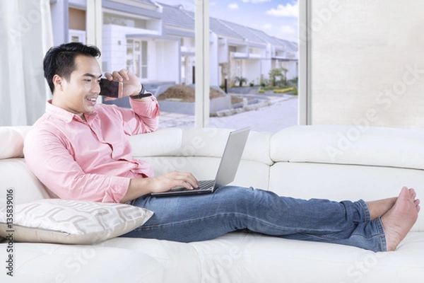Fototapeta Handsome man talks on cellphone at couch