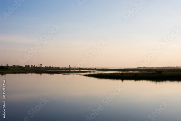 Fototapeta The sky in orange and blue shades is reflected on the water of the river.