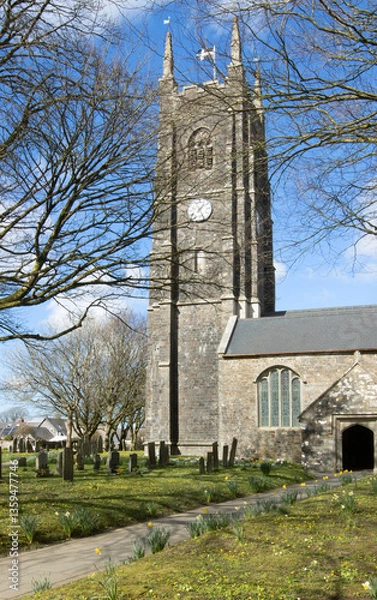 Fototapeta 15th Century Norman 'St James the great' church with clock tower and Cornish flag in Kirkhampton in Cornwall during spring