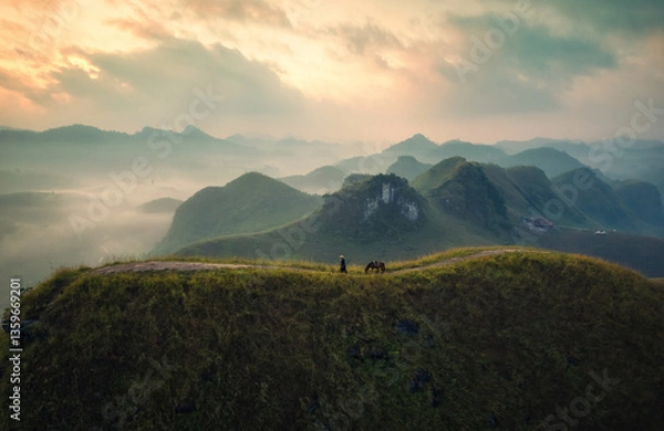 Fototapeta Scenery of Ba Guang grass hill, Mountain range with fog and villager bringing horse to graze on the mountain in the morning