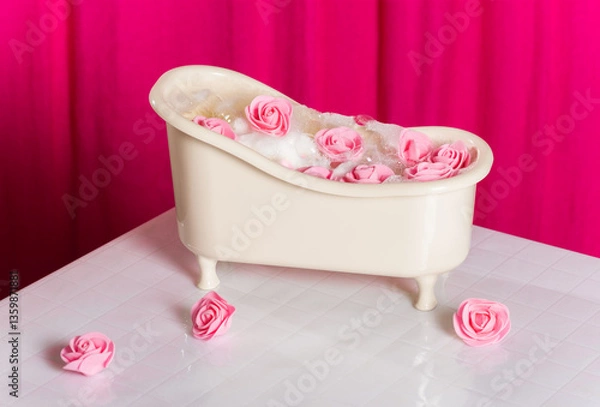 Fototapeta Creative spa card. Miniature bath tub with pink roses on a background of white tiles and pink curtains.