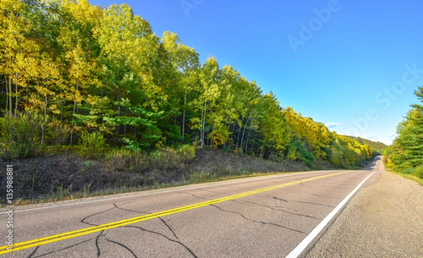 Fototapeta Summer highway open road to anywhere.
Sunny blue sky, woods on either side down a country highway in summer.  