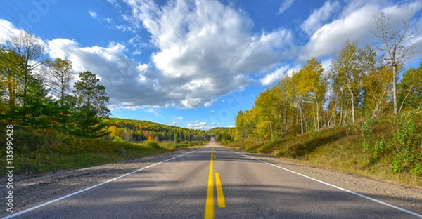 Fototapeta Sunny road to anywhere, single point perspective down a country highway in summer.  Warm day to drive or travel to anywhere. 