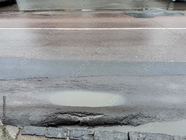 Fototapeta Damaged asphalt road with a large puddle and pothole after rain. Common urban infrastructure issue, representing poor road maintenance and weather impact. High quality photo