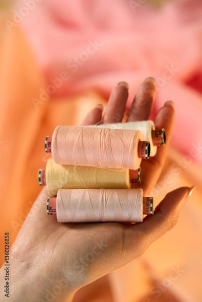 Obraz Hand holding Raw White Polyester FDY Yarn spool, Polyester Filament Yarn spool.PET fiber Yarn,spun polyester sewing thread with peach background.