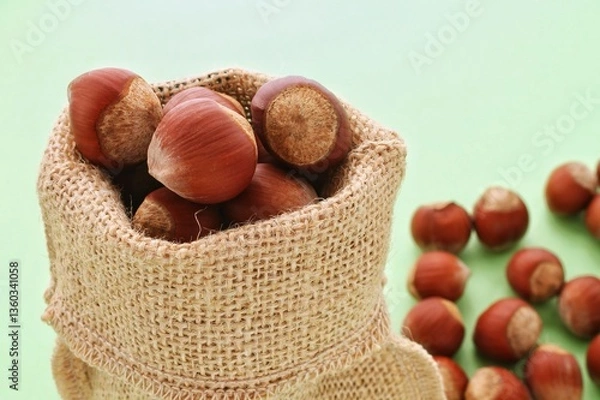 Obraz Hazelnuts overflowing from burlap sack on surface. Close-up of hazelnuts in jute bag. Many whole hazelnuts in natural fabric bag. Nuts inside and around sack. Pile of hazelnuts with burlap container