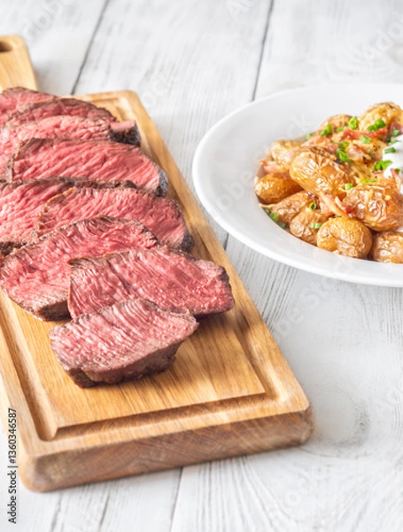 Obraz Juicy medium-rare steak with baked potatoes, crispy bacon, and melted cheddar