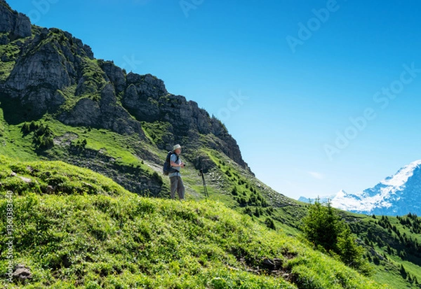 Obraz Switzerland travel - Senior man backpack hiking the Swiss Alps looking at view at Schynige Platte and the snowcapped mountains in the Jungfrau region
