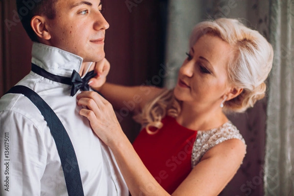 Fototapeta Mother is helping with a bow-tie to her son before wedding ceremony. Concept mother and son.