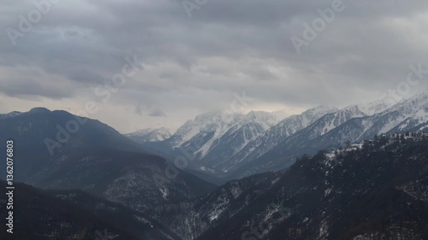 Fototapeta Snow-covered mountain range under grey sky, power lines visible, serene wintry landscape.