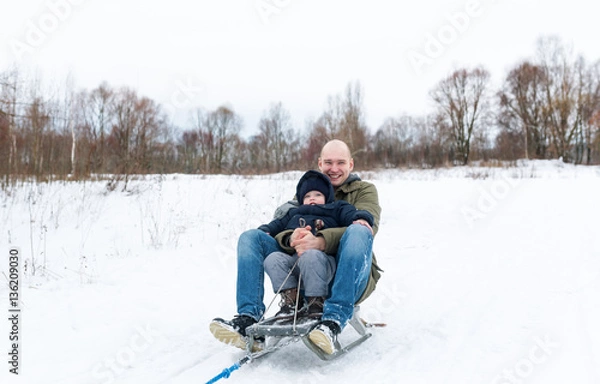 Fototapeta Young man with the little boy sitting on sledge in snow