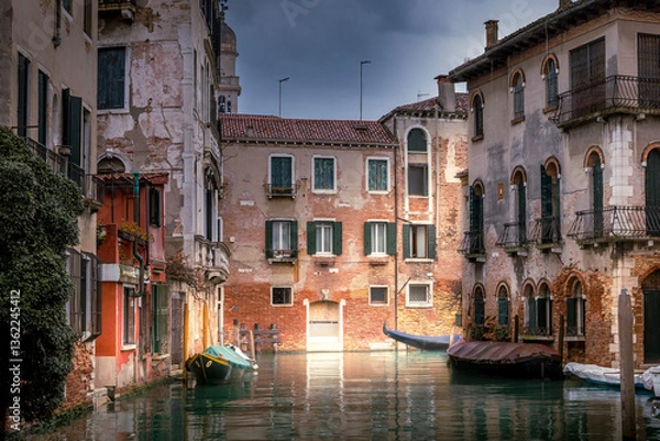 Fototapeta Venice, Italy - February 10, 2024: A tranquil canal scene in Venice, with weathered buildings lining the water, and boats moored alongside