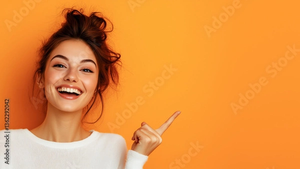 Obraz Beautiful girl posing on orange background and pointing finger at place for advertisement and text