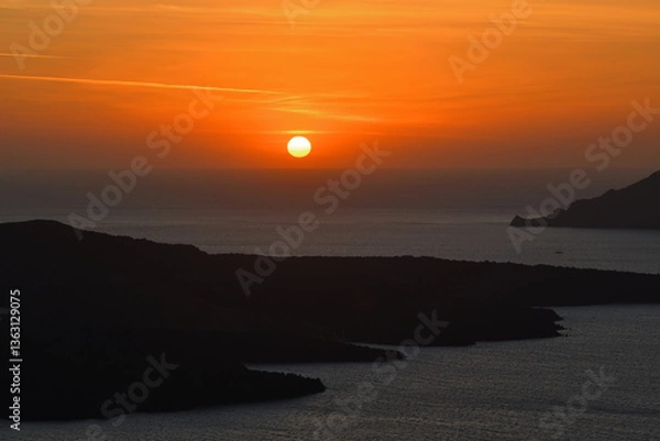 Obraz Die Sonne versinkt am Horizont wunderschön ins Meer, während im Vordergrund man noch die Inseln von Santorini sieht.