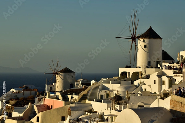 Obraz Die berühmten Windmühlen von Oia auf der Griechischen Insel Santorini stehen im warmen Abendlicht, und im Hintergrund sieht man das Blaue Meer