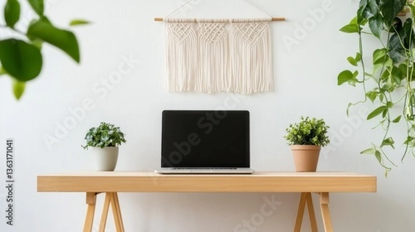 Fototapeta Laptop with blank screen sits on light wood desk, flanked by potted plants, against a white wall with macrame wall