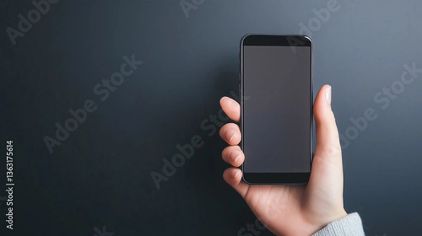 Fototapeta A hand holds a black smartphone against a muted gray background revealing modern digital simplicity