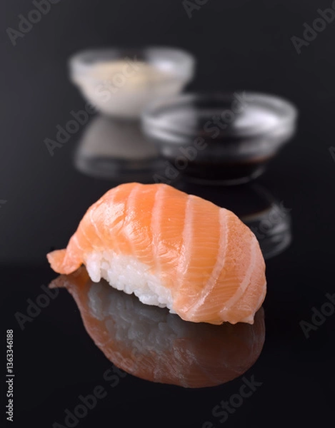 Fototapeta Salmon nigiri reflecting on dark surface with soy sauce and wasabi