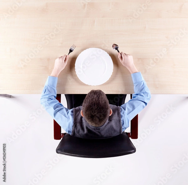 Fototapeta Boy sitting in a chair at the office table with tableware. Top view.