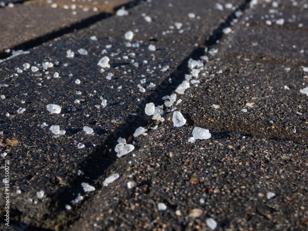 Fototapeta Close-up of white salt grains on icy sidewalk surface in the winter. Applying salt to keep roads clear and people safe in winter